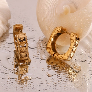 Macro shot of 18K gold-plated square hoop earrings with embossed heart patterns on water