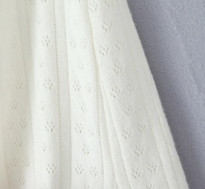 Vue détaillée du tissu en maille blanche avec rayures verticales et motifs ajourés