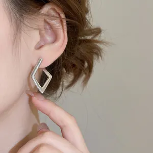 Minimalist geometric rhombus huggie hoop earrings in silver finish worn by a model