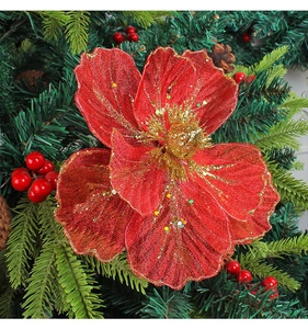 Detail of red mesh Christmas flower with gold sequins on green pine tree branch