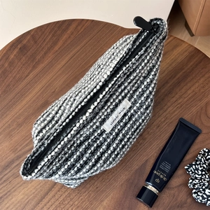 Detail of black and white tweed cosmetic bag with 'simple wish' label on wood surface