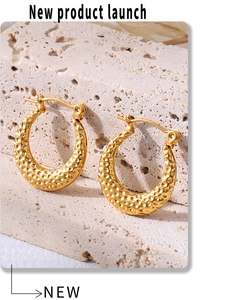 Macro shot of gold C-shaped earrings with hammered texture on a neutral stone background