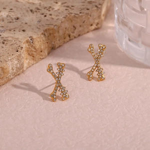 Detail of gold X-shaped earrings with micro-paved rhinestones on a textured background