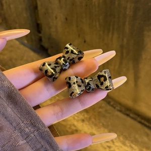 Handheld view of vintage leopard print bow earrings with sparkling glitter finish
