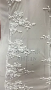 Detailed view of white tulle fabric featuring intricate 3D floral embroidery on a gown