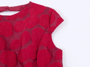 Détail d'une robe bordeaux montrant le tissu jacquard rose 3D et le bouton au cou