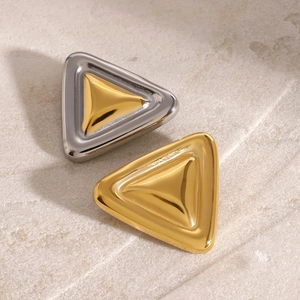 Detail of geometric chunky metal brooches in silver and gold on a stone background