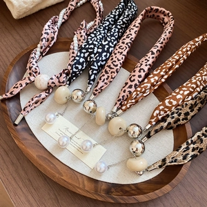 Détail de colliers foulards en soie léopard avec perles et résine sur plateau bois