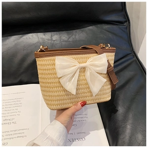 Close-up of woven straw bucket bag with a large chiffon bow and leather strap detail