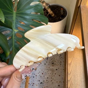 Close-up of a large cream marble acetate hair claw clip held in hand with plant background