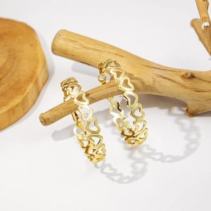 Detailed view of gold heart-shaped hollow earrings hanging on a natural wooden branch