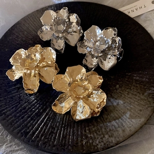 Macro detail of textured gold and silver metal flower stud earrings on a dark tray