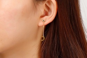 Detail of a model wearing long gold-colored earrings with star studs and moon pendants