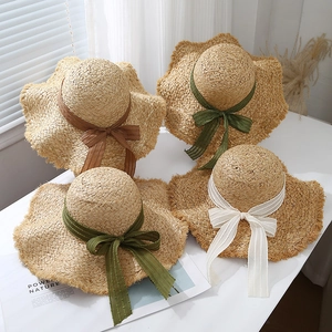 Detail of wavy brim raffia sun hats with four colorful striped ribbon bows on white surface