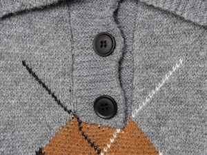 Dettaglio del cardigan grigio con motivi geometrici e bottoni neri opachi rotondi