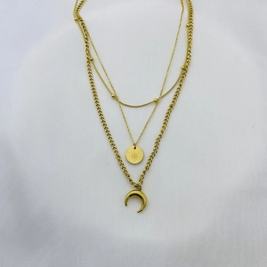 Detailed close-up of triple-layered gold necklace with moon and star pendants on white fabric