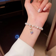 Close-up of pearl bead bracelet with transparent heart charm worn on a female wrist