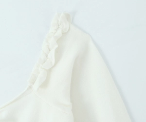 Detail of the ruffle edge on the square neck and fine texture of the white knit top