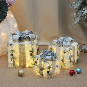Close-up of three white lighted Christmas gift boxes with pine cones and warm LED lights