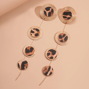 Golden drop earrings with textured leopard print discs and fine chains on beige background