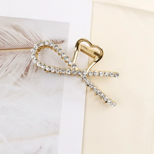 Close-up of elegant gold alloy hair claw clip with sparkling rhinestones in a ribbon design