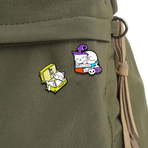 Cute magic cat enamel pins and luggage cat badge displayed on a green canvas backpack