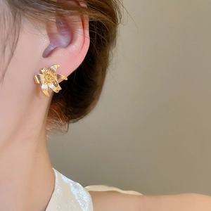 Detail view of golden lily flower stud earring worn by model with textured metal petals