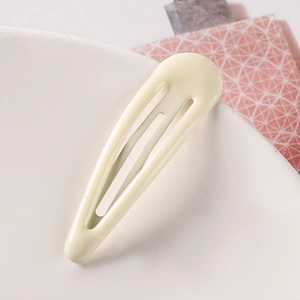 Macro shot of a cream yellow snap hair clip with a glossy finish on white ceramic