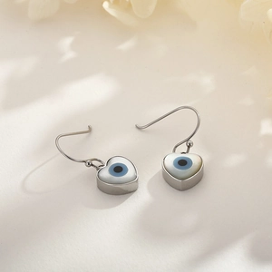 Detail shot of silver heart earrings with shell inlay and blue evil eye design