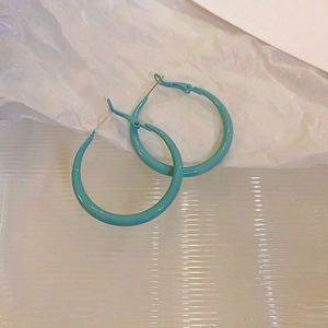 Detail of light blue geometric hoop earrings with smooth matte finish on a textured background