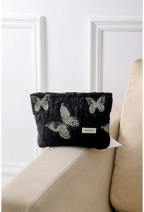 Close-up of black fabric makeup bag with silver butterfly embroidery and woven logo label