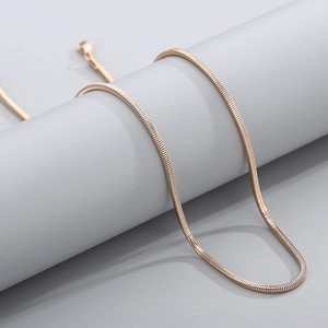 Chic rose gold square snake bone necklace draped on a minimalist gray pedestal