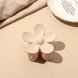 Close-up of cream matte floral claw clip on white porcelain plate with silk texture
