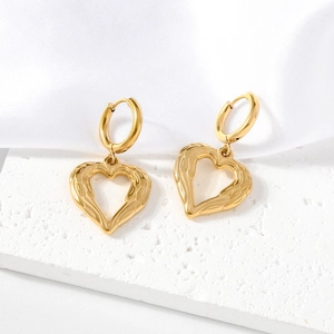 Boucles d'oreilles cœur ailé en acier doré 18K avec texture en relief sur fond de soie