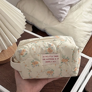 Detail of floral quilted cotton makeup bag with metal zipper and woven handle strap