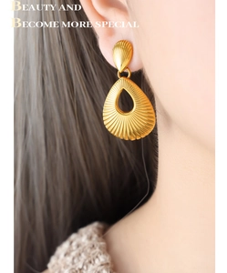 Close-up of gold hollow teardrop earrings with textured shell patterns on model