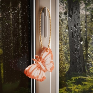 Orange butterfly pendant with gold chain hanging on window with rainy forest background