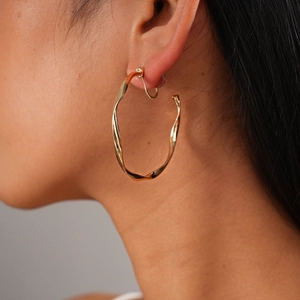 Close-up of model wearing large twisted gold hoop earrings with metallic texture