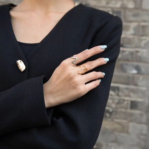 Detail of model wearing gold heart ring, silver S-curve ring, and gold brooch on blazer