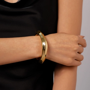 Detailed view of irregular wavy gold bracelet with polished finish on woman's wrist