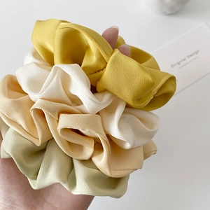 Elegant satin scrunchies in pastel yellow and green on a minimalist white background