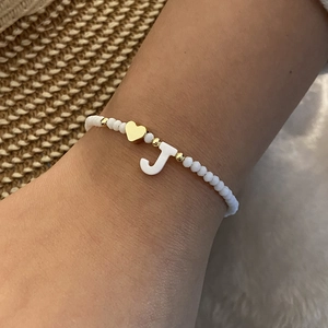 Detail of white beaded bracelet with gold heart charm and shell-style letter J pendant