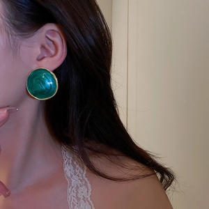 Close-up of vintage green enamel round earring with gold trim on a female model's ear