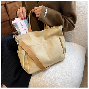 Close-up of canvas tote bag with front pockets and brown woven adjustable strap