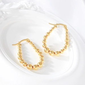 Polished gold beaded oval hoop earrings in stainless steel on a white tray