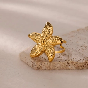 Dettaglio dell'anello stella marina dorata con texture granulate su pietra beige