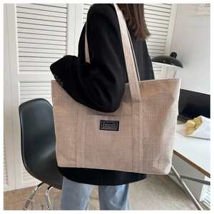 Detail of a beige canvas tote bag with a woven texture and fashion label detail