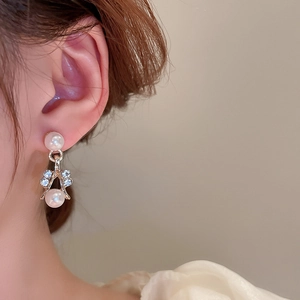 Close-up of gold pearl earrings with rhinestones worn by a model in soft light