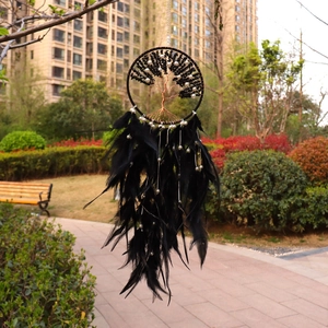 Handmade black dream catcher with golden tree of life and feathers hanging in a garden