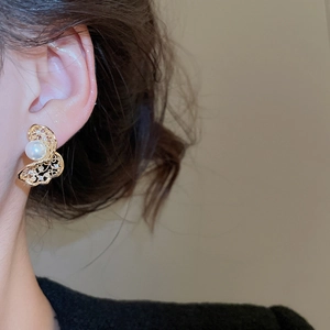 Detail shot of a golden hollow butterfly earring with pearls on a model ear